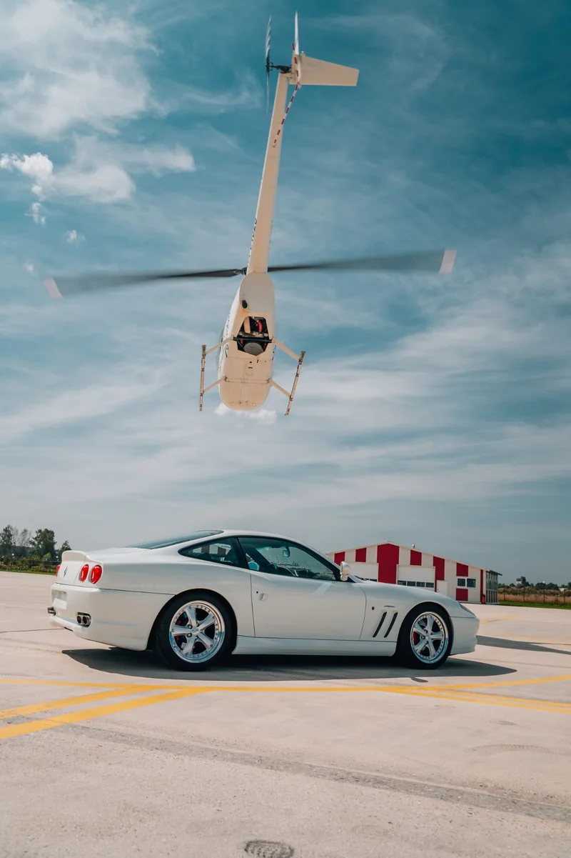 Helicopter in flight above an apron with a white sports car